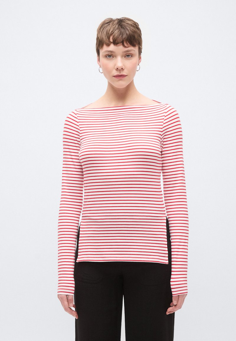 Hosszú ujjú, fehér alapon piros vízszintes csíkos ing, hajónyakú kivágással és oldalsó hasítékokkal a könnyű mozgás érdekében.