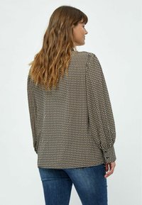 Long-sleeved blouse in a geometric black and cream pattern. Features gathered shoulder details and fitted cuffs. Paired with blue jeans.