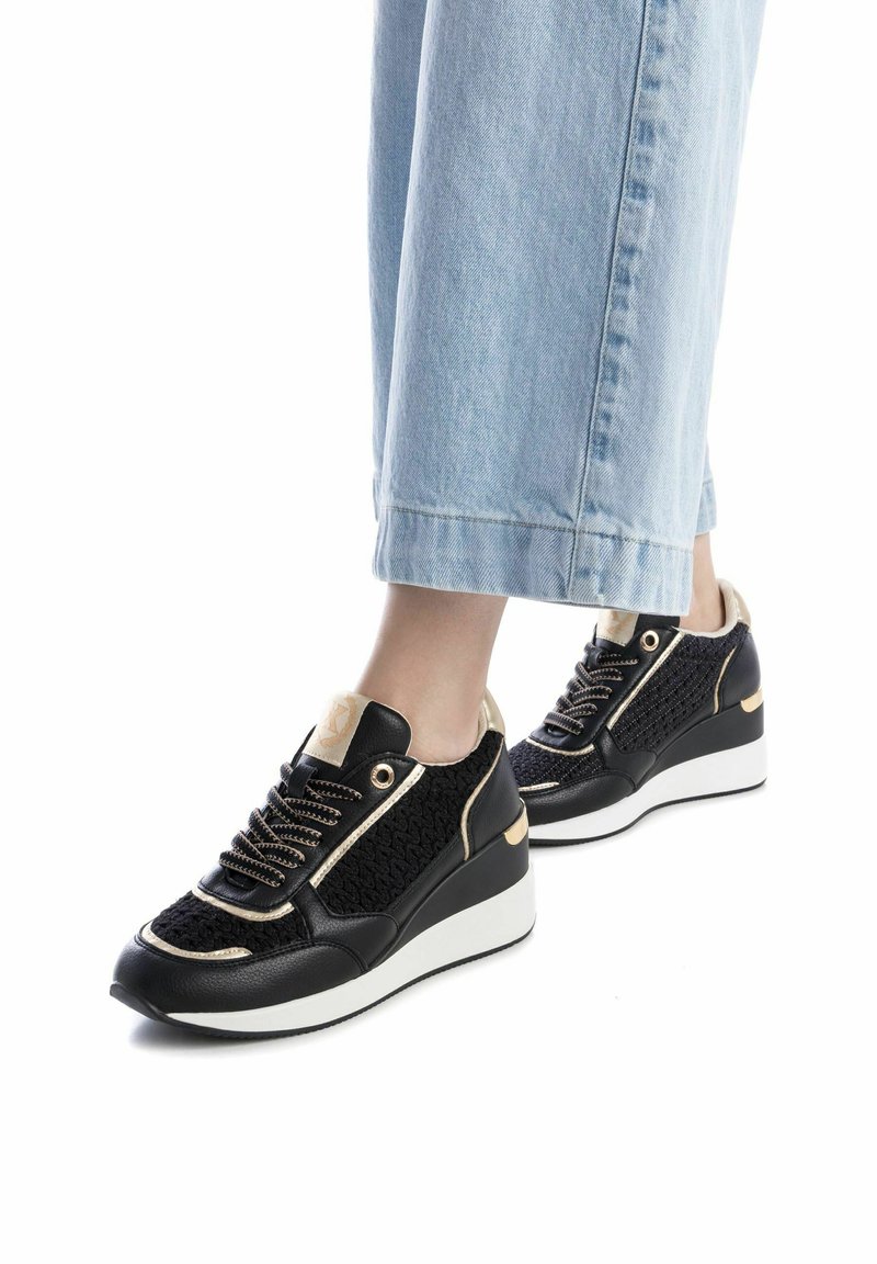 Zapatillas negras y doradas con textura trenzada, cuero contrastante, cordones planos, ojales redondos dorados y una suela blanca gruesa.
