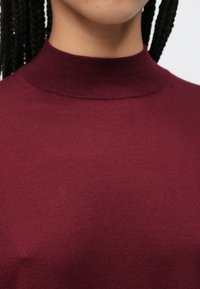 Pulover visiniu cu guler înalt, confecționat din țesătură tricotată cu nervuri, cu un croi mulat, textură netedă și detalii subtile de cusătură.