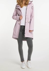 Ljuslila regnjacka med huva, två sidofickor, dragkedjestängning, justerbara dragsnören och tryckknappar; tillsammans med grå jeans och vita sneakers.