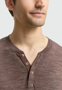 Bruine henley shirt met een gestructureerde stof, drie knopen en een contrasterende rode stiksel langs de placket. Casual stijl.