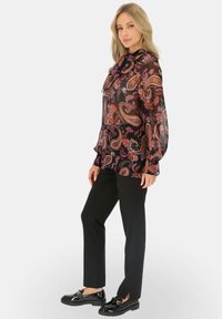 Czarna bluzka w wzór paisley z długimi rękawami i wiązanym dekoltem, zestawiona z czarnymi spodniami i lakierowanymi loafersami, prezentując teksturowany, płynny design.