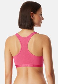 Racerback bralette in een levendige roze stof met een gladde textuur. Heeft een tonale logoband aan de onderkant en een aansluitend ontwerp.
