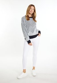 Maglione lavorato a maglia con motivo a zig zag in blu navy, bianco e nero, con orlo e polsini a coste, abbinato a jeans skinny bianchi e sneakers bianche.