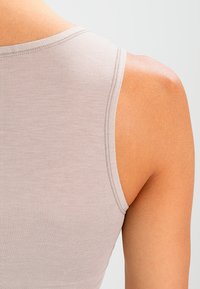 Light gray tank top featuring a seamless design, soft texture, and smooth fabric, with a rounded neckline and wide shoulder straps.