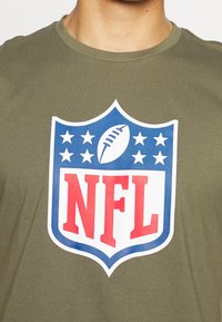 Khaki zelené tričko z bavlny, s velkým logem NFL a červeným textem na modrém pozadí ve tvaru štítu, obklopené bílými hvězdami.