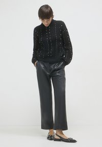 Schwarzer Strickpullover mit erhobenen Kabelmustern und Perlenakzenten, kombiniert mit hoch taillierten schwarzen Leder-Hosen in weitem Schnitt und schwarzen Slingback-Ballerinas.