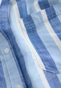 Tissu de chemise en coton rayé bleu et blanc avec une poche avant et des boutons blancs en gros plan.