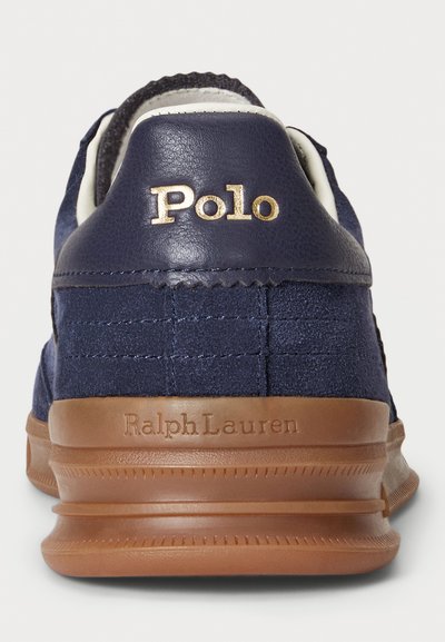 Navy blue sneaker with suede and leather heel, brown rubber sole embossed with "Ralph Lauren," gold "Polo" logo on back collar.