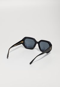 Black octagonal sunglasses with dark lenses and gold accents on the temples. Features sleek, polished frames and textured detail on arms.
