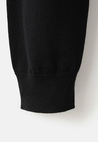 Manica in tessuto nero lavorato a maglia con polsino a coste, mostrata su uno sfondo neutro chiaro.