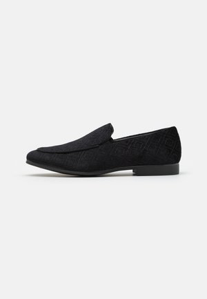 Mocassin noir texturé à enfiler avec petit talon et bout pointu, présenté en profil latéral sur fond blanc.