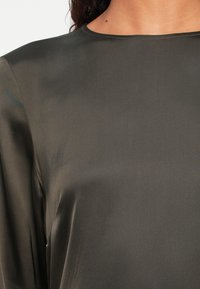 Tuvo plāns, kur cilvēks valkā tumši pelēku garām piedurknēm satīna blūzi ar apaļu dekoltē un gludu tekstūru.