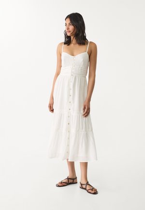 White cotton sundress with adjustable spaghetti straps, button front, and tiered skirt. Features subtle gathering and lace details.