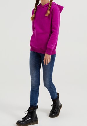 Sweatshirt à capuche fuchsia avec poche kangourou, poignets et ourlet côtelés. Associé à un jean bleu et des bottes noires à lacets.