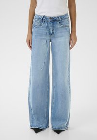 Person wearing light blue wide-leg jeans with a thin denim belt, paired with black pointed shoes and a white top.