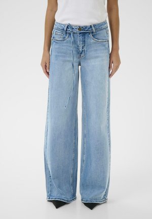 Person wearing light blue wide-leg jeans with a thin denim belt, paired with black pointed shoes and a white top.