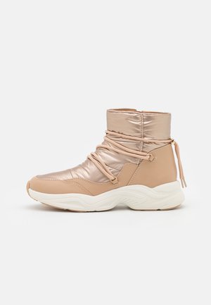Bottine beige matelassée avec semelle blanche épaisse et lacets enveloppés, conçue pour un port hivernal décontracté.