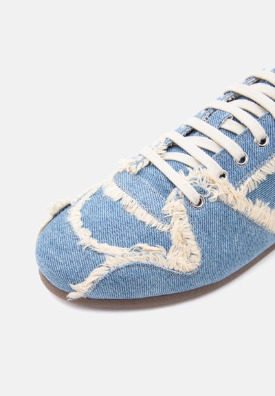 Baskets en denim avec bords effilochés, lacets blancs et œillets métalliques, montrant les détails du tissu texturé et des coutures de la chaussure.