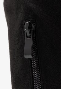 Gros plan d'un curseur de fermeture éclair en plastique noir sur un vêtement en tissu noir, montrant les dents de la fermeture éclair et la surface texturée du tissu.