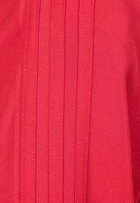 Roter Stoff mit vertikalen Falten und einer strukturierten Oberfläche. Genähte Nähte verleihen dem Design Detail.