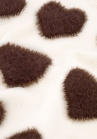 Gebreide stof met fuzzy bruine hartvormen op een crèmekleurige achtergrond. De harten hebben een gestructureerd, pluizig oppervlak en zichtbare randen.