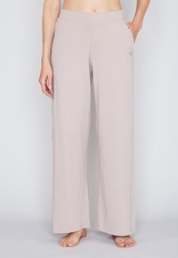 Helle beige weite Hosen aus weichem Material, mit Seitentaschen und einem kleinen floralem Stickdetail auf der linken Seite.