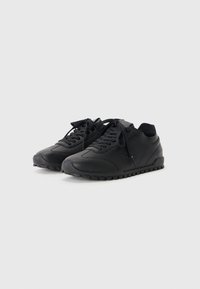 Black sneakers made of smooth leather with a textured rubber sole, featuring flat laces, subtle branding, and rounded toe design.