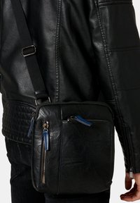 Borsa a tracolla in pelle nera con due tasche con zip, dettagliata con accenti blu e una superficie testurizzata. Cinghia regolabile inclusa.
