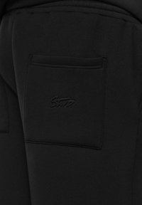 Gros plan sur une poche en tissu noir avec un logo cousu portant l'inscription "Star" sur un détail de vêtement.