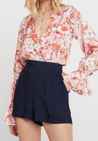 Blouse fleurie aux tons roses et pêche avec manches longues évasées, associée à un short taille haute bleu marine avec ourlet retourné.
