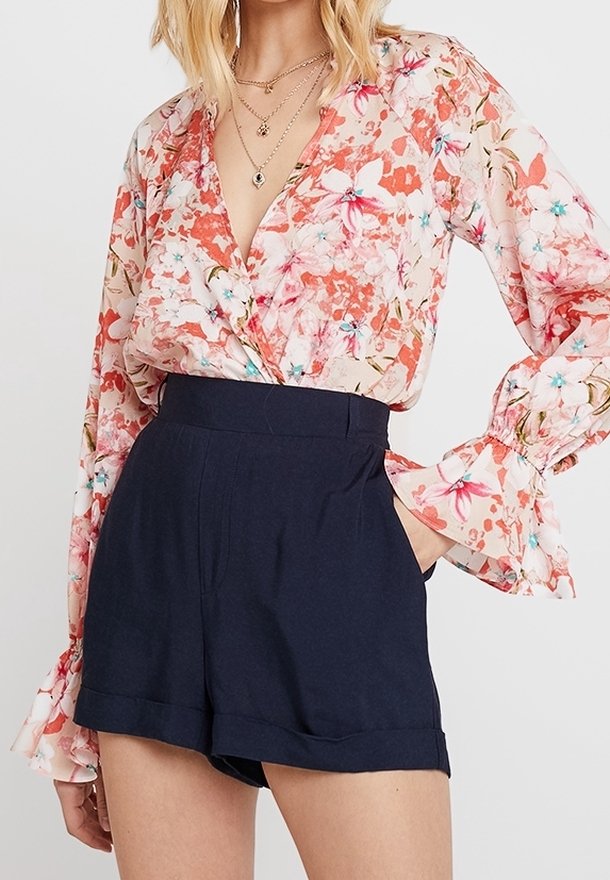 Blouse fleurie aux tons roses et pêche avec manches longues évasées, associée à un short taille haute bleu marine avec ourlet retourné.