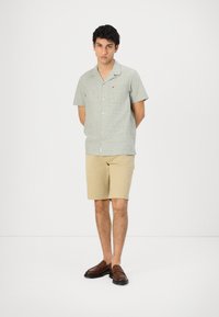Groen korte mouw button-up shirt met een borstzak en een klein logo, gecombineerd met beige shorts en bruine instap schoenen. Eenvoudig ontwerp.