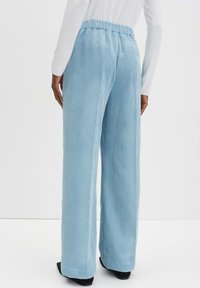 Pantalons en velours côtelé bleu clair avec une coupe décontractée, une taille élastique et des jambes larges. Pas de poches visibles ni de détails supplémentaires.