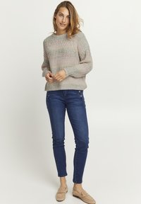 Strickpullover mit Textur in Pastelltönen, entspannte Passform. Kombiniert mit dunkelblauen Skinny-Jeans und beigen Loafers, die einen lässigen Look zeigen.
