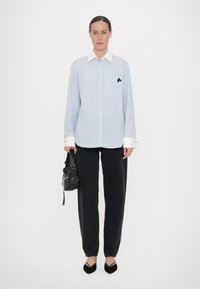 Light blue striped button-up shirt with a white collar, paired with dark jeans and a black textured bag, featuring pointed black flats.