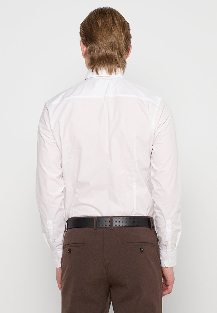 Camisa de botón de manga larga color rosa claro exhibida desde la parte de atrás, con una textura suave, cuello puntiagudo y cinturón marrón en contraste.