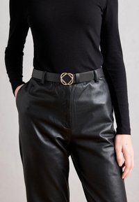 Curea din piele neagră cu o cataramă ovală de ton auriu unică. Împerecheată cu pantaloni din piele neagră și o bluză neagră cu mânecă lungă. Contrast elegant.
