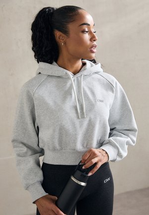 Light grey cropped hoodie with a drawstring hood and ribbed cuffs, paired with black leggings. The person holds a black water bottle.
