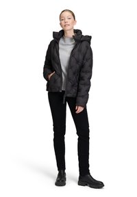 Czarna kurtka puchowa z kapturem, z pikowanym wzorem, bocznymi kieszeniami i zapięciem na zamek, noszona na szarym swetrze i czarnych spodniach.