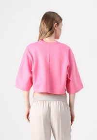 Pink cropped sweatshirt with short sleeves, featuring a round neckline and seam detail at the back. Worn with beige, elastic waistband pants.