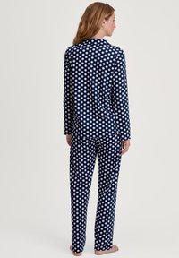 Navy blauwe pyjama set met stippen, bestaande uit een langemouwen top en broek. Zachte stof met een gladde textuur, geaccentueerd met witte cirkelvormige patronen.