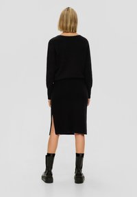 Svart stickad tröja och kjolset med en sidospalt, med långa ärmar och avslappnad passform, ihop med svarta ankelskor.