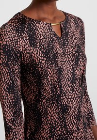 Robe à manches longues en tissu noir à motif de pois roses, dotée d'un décolleté en trou de serrure avec un accent doré et une texture lisse.