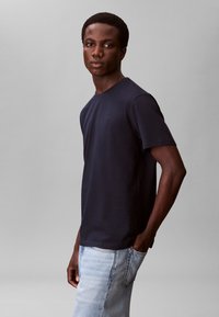 Marineblå bomuld t-shirt med korte ærmer, rund halsudskæring og diskret logodetalje. Kombineret med lyseblå denimjeans.