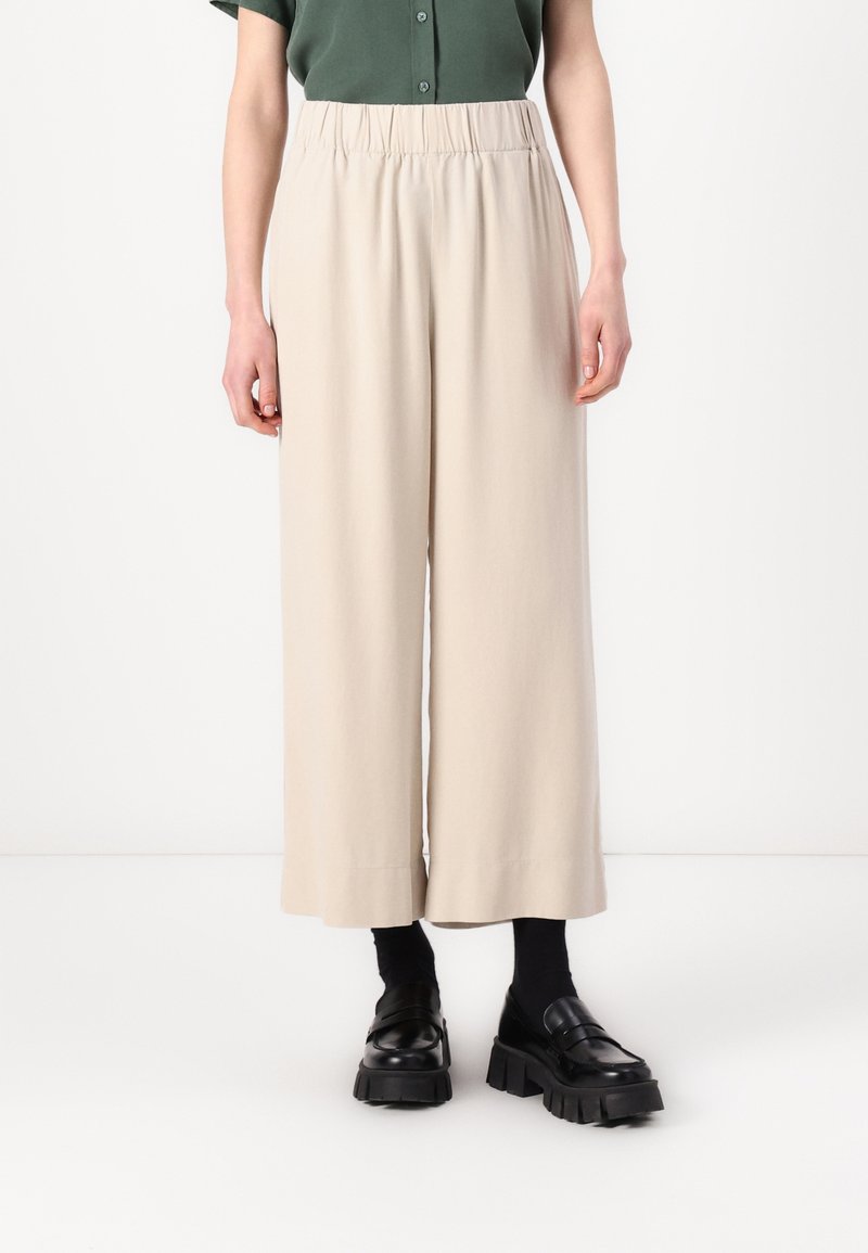Beige wide-leg pants made of soft fabric, featuring an elastic waistband. Styled with black chunky loafers and black socks.