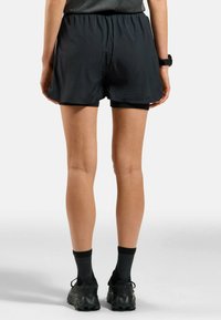 Zwarte sport shorts met een elastische tailleband, gemaakt van een lichte stof en met een losse pasvorm. Gepaard met zwarte hardloopschoenen en sokken.