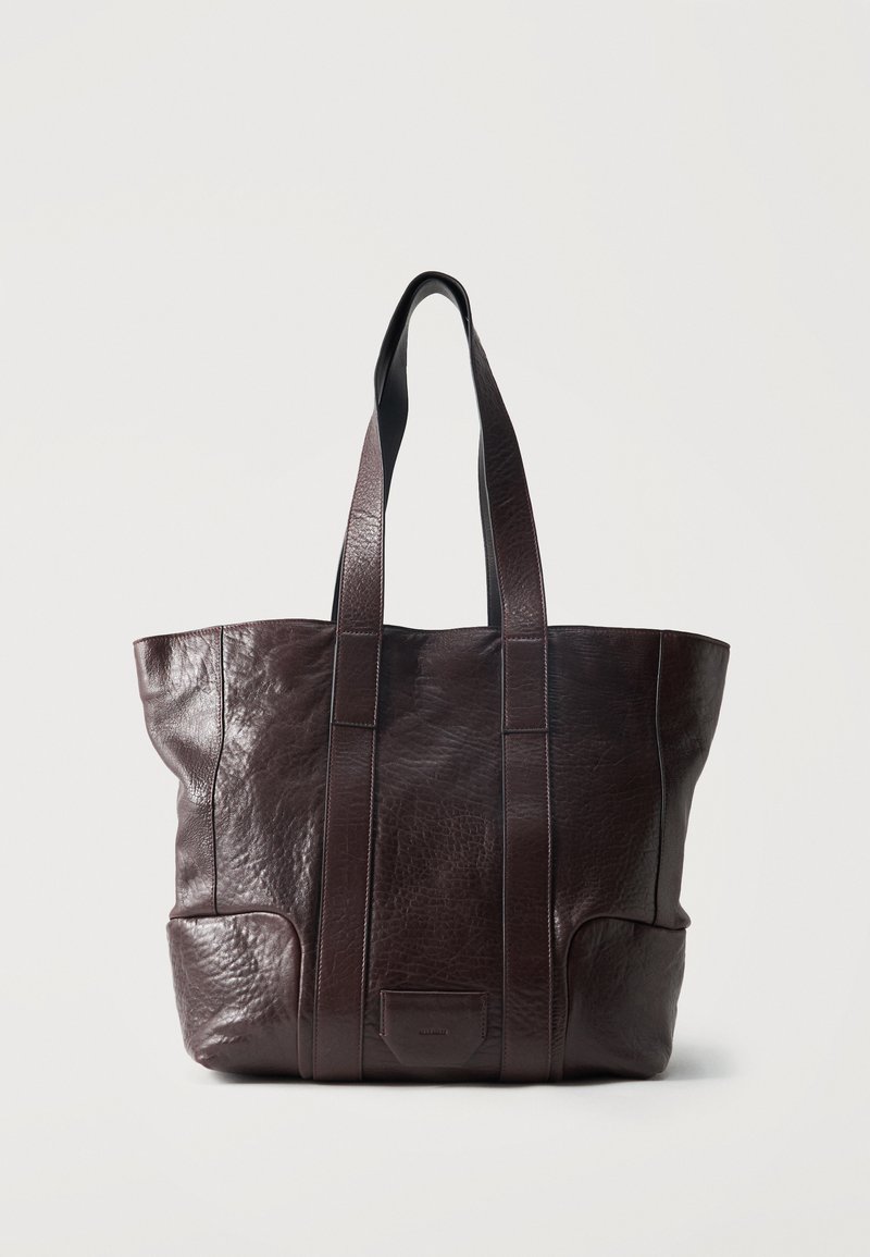 Σκούρο καφέ δερμάτινη τσάντα tote με μακριές λαβές και υφασμένη επιφάνεια, όρθια σε απλό ανοιχτό φόντο.