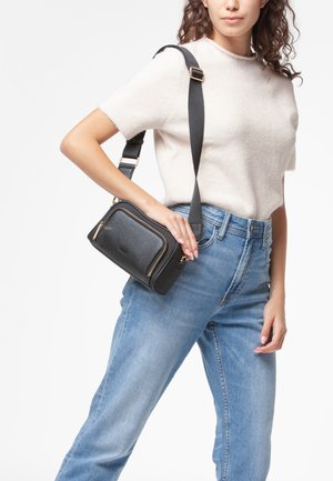 Borsa a tracolla in pelle nera con finitura martellata, dettagli in metallo dorato sulle cerniere e tracolla in tessuto regolabile, indossata da un modello.